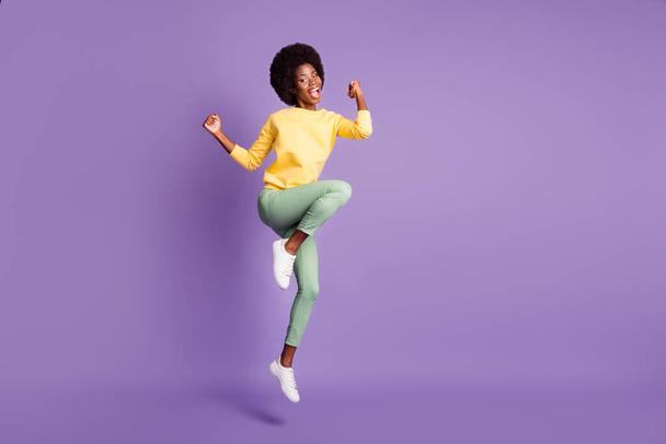 Full length photo of crazy afro american girl jump raise fists wear yellow pullover isolated over violet color background - Foto, Imagem