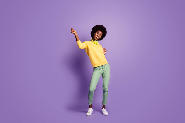 Full length photo of cute young woman raise hands wear earphones yellow sweater isolated violet color background - 写真・画像
