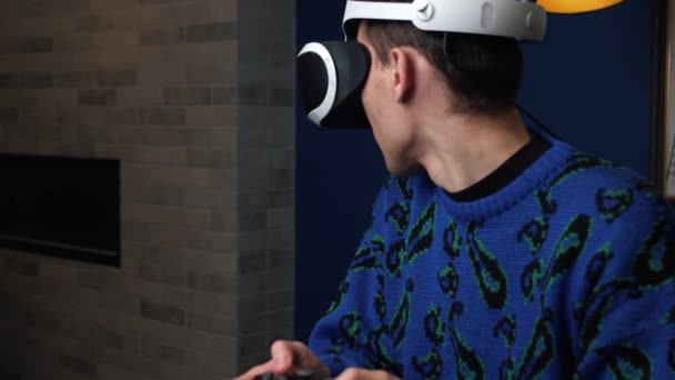 Atractivo hombre caucásico emocionado sostener joystick y usar gafas de realidad virtual casco de auriculares en el sofá en casa. Felicidad gamer jugando juego usando gafas VR en casa. - Imágenes, Vídeo