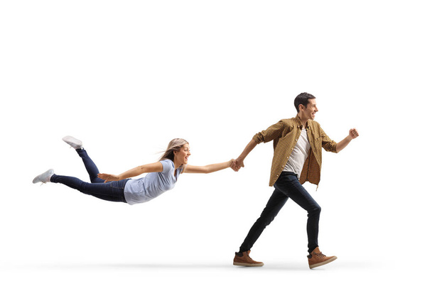 Full length profile shot of a casual man running and holding a woman with his hand isolated on white background - Fotoğraf, Görsel