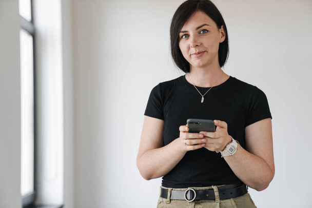 Mosolygó fiatal nő használ mobiltelefon otthon, SMS - Fotó, kép