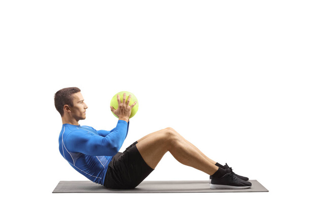 Young man in sportswear exercising with a ball on the floor on an exercise mat isolated on white background - Фото, зображення