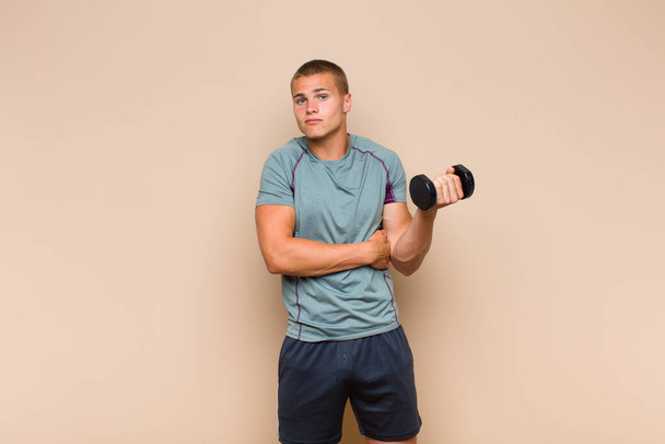 young blonde man shrugging, feeling confused and uncertain, doubting with arms crossed and puzzled look - Photo, image