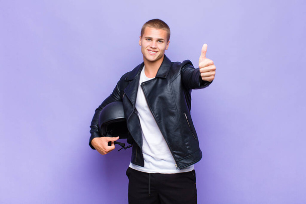 young blonde man feeling proud, carefree, confident and happy, smiling positively with thumbs up - 写真・画像