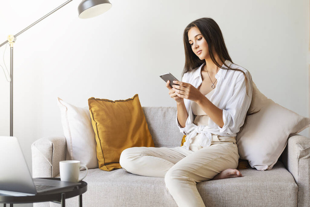 Female relaxing at home, using smartphone to text messages, share photos, communicate with friends, check email - Foto, imagen