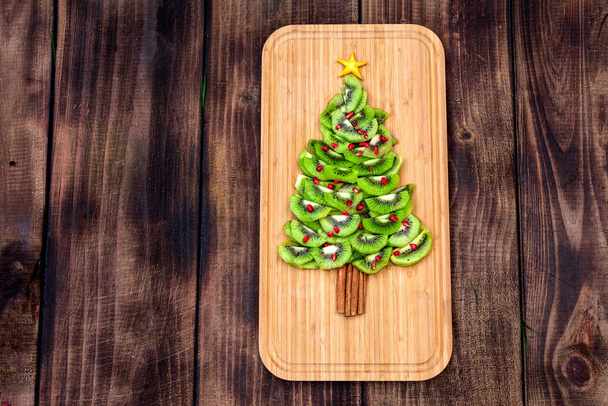 Kiwi Christmas tree - fun food idea for kids party or breakfast, New Year food on wooden background. Christmas tree food concept. Flat lay. Top view. - Photo, image