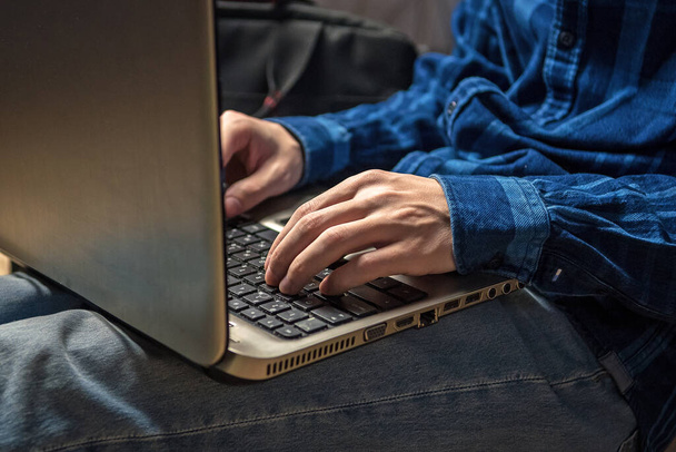 Um homem está digitando em um laptop enquanto está sentado no sofá. - Foto, Imagem