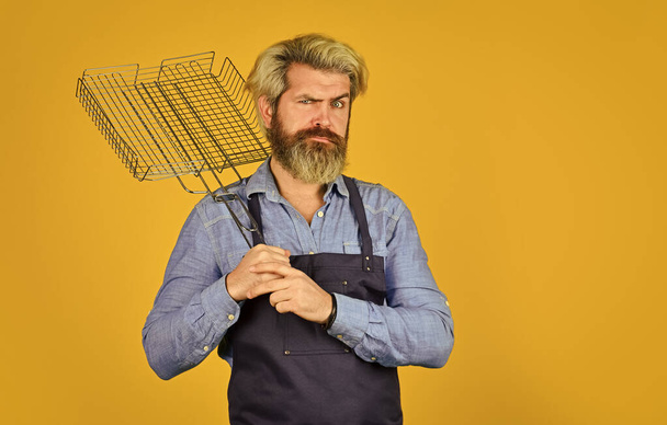 Tools for roasting meat. Man in apron hold barbecue grill. Chef cooking bbq food. Summer picnic. Hipster dyed beard promoting bbq equipment. Cooking healthy. Culinary concept. Cooking utensils - Foto, Imagen