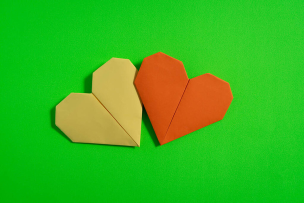 Origami hartjes gemaakt met gekleurd papier voor felicitaties op Valentijnsdag voor verliefde paren, met groene achtergrond. Liefde concept - Foto, afbeelding