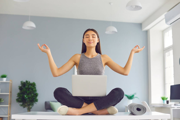 Office worker with positive mindset sitting on desk in easy pose meditating and relaxing - Photo, Image