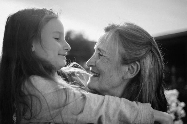 Portrait noir et blanc de grand-mère aînée aux cheveux gris avec sa petite-fille étreignant dans le jardin et pendant la journée ensoleillée en plein air, fête des mères - Photo, image