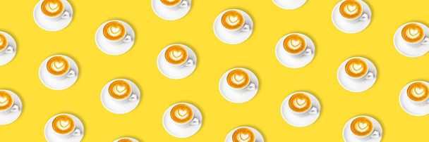 Pattern of white cup of cappuccino with latte art on yellow background. - Photo, Image