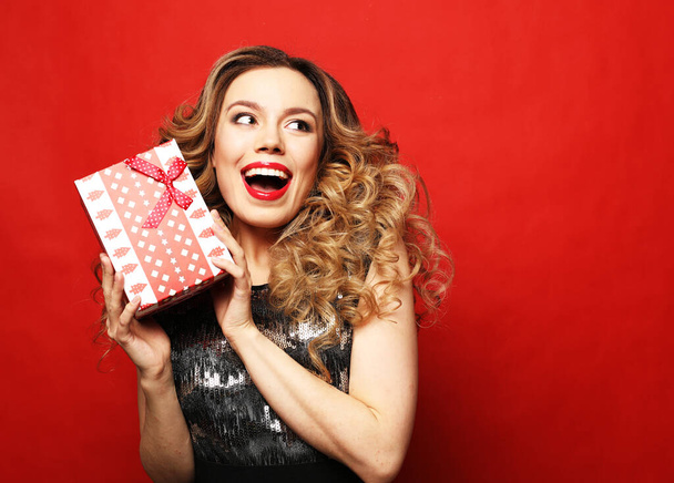 New Year, Birthday, holiday concept: Portrait of a happy smiling woman in dress holding present box isolated over red background - Photo, Image