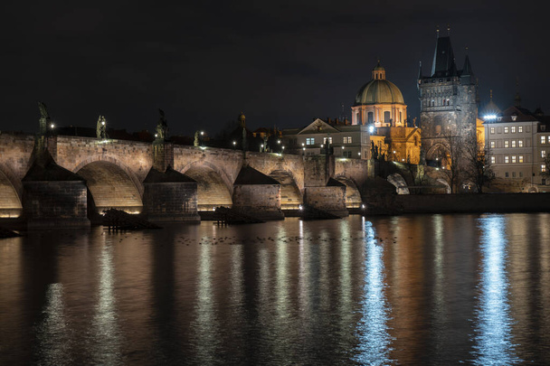 stary oświetlony kamień Most Karola i światła uliczne odbijają się na powierzchni Wełtawy w centrum Pragi w nocy w Republice Czeskiej - Zdjęcie, obraz