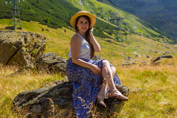 chica en vestido se sienta en una roca sosteniendo un sombrero de paja - Foto, imagen