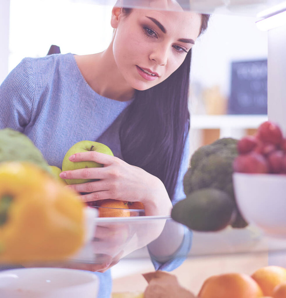 Smiling woman taking a fresh fruit out of the fridge, healthy food concept. - Photo, image