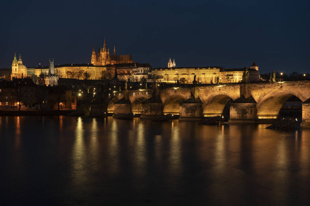 régi kivilágított prágai vár és Károly híd és Szent vita templom fények utcai lámpák tükröződnek a felszínen a Moldva folyó központjában Prágában éjjel a Cseh Köztársaságban - Fotó, kép