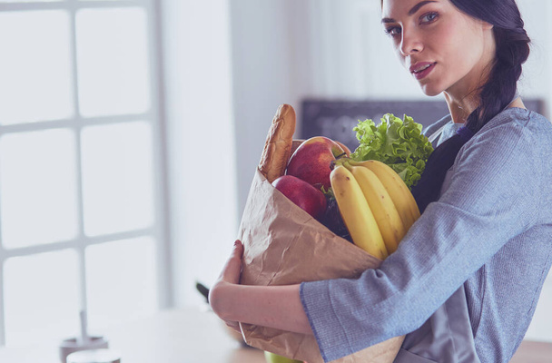 Young woman holding grocery shopping bag with vegetables .Standing in the kitchen - Foto, Imagem