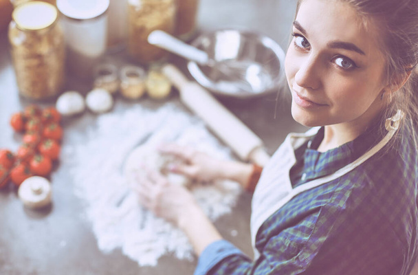 Beautiful woman cooking cake in kitchen standing near desk - Foto, afbeelding