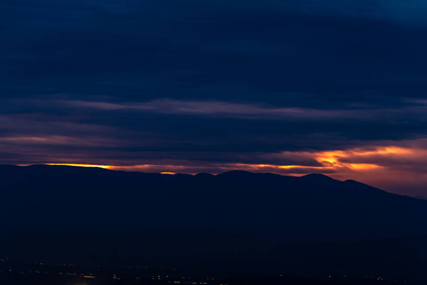 Ostatnie promienie słońca wśród ciemnoniebieskich chmur nad miastem górskiego krajobrazu - Zdjęcie, obraz