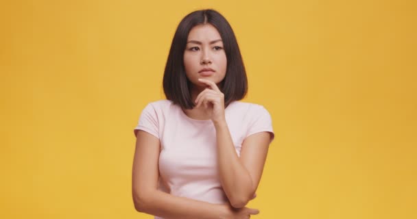 Jovem pensativo asiático mulher ponderando sobre algo, tocando seu queixo, laranja estúdio fundo - Filmagem, Vídeo