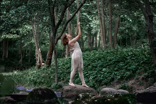 A young beautiful woman in a dress stands barefoot on a rock and dances. - 写真・画像