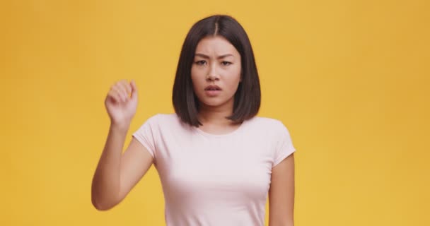 Ontevreden jonge aziatische vrouw zeggen nee, tonen stop gebaar met palm, oranje studio achtergrond - Video