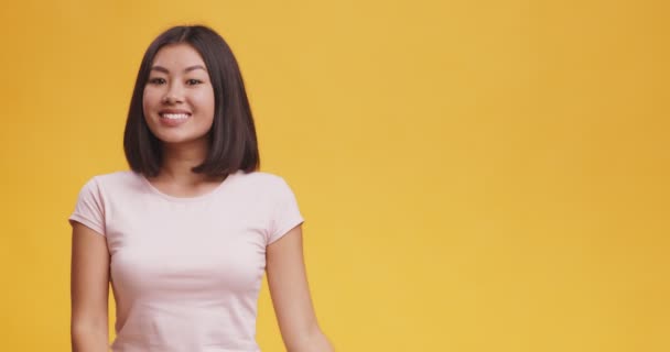 Allegro asiatico donna positivamente indicando da parte a copia spazio, arancio studio sfondo, mock up - Filmati, video