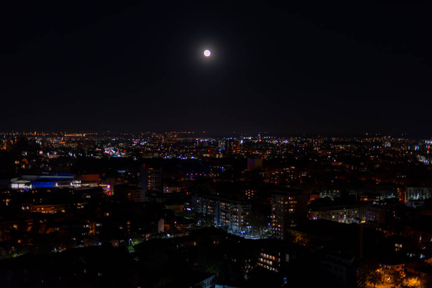 Wielkie ciemne miasto oświetlone światłem księżyca i tysiące małych świateł wysoki punkt widzenia od szczytu wzgórza w nocy - Zdjęcie, obraz