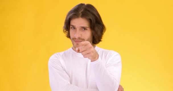 Young playful guy pointing at camera and showing phone gesture, flirting with you over orange studio background - Footage, Video