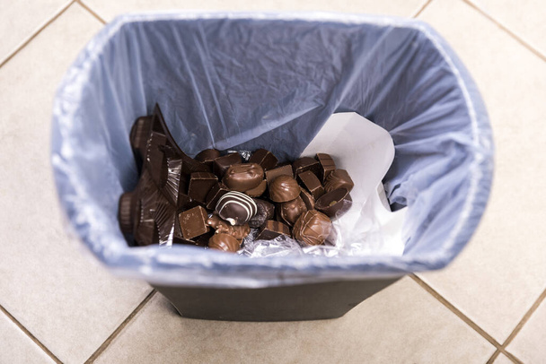 Tentar chocolates poco saludables eliminados en un cubo de basura al comienzo de una dieta - Foto, Imagen