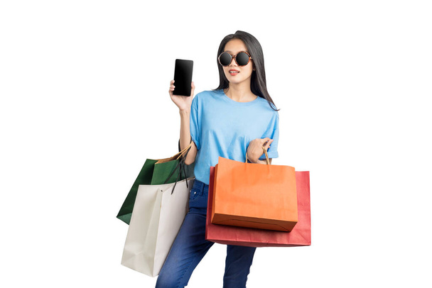 Asian woman with sunglasses carrying shopping bags holding mobile phone isolated over white background - Valokuva, kuva