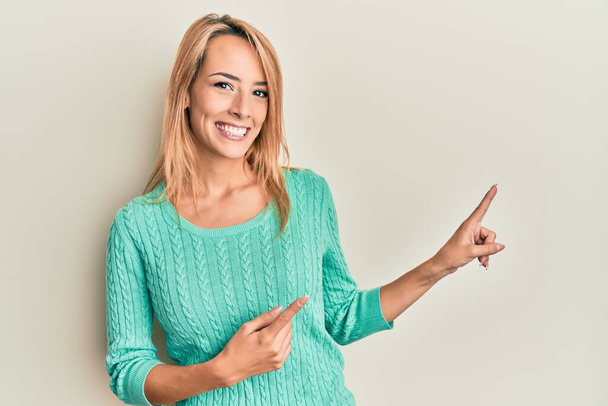 Mooie blonde vrouw dragen casual winter trui glimlachen en kijken naar de camera wijzen met twee handen en vingers naar de zijkant.  - Foto, afbeelding