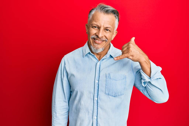 Middle age grey-haired man wearing casual clothes smiling doing phone gesture with hand and fingers like talking on the telephone. communicating concepts.  - Photo, Image