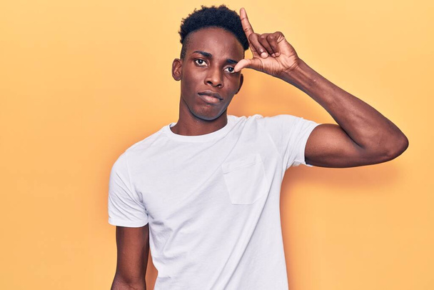 Young african american man wearing casual clothes making fun of people with fingers on forehead doing loser gesture mocking and insulting.  - Foto, Bild