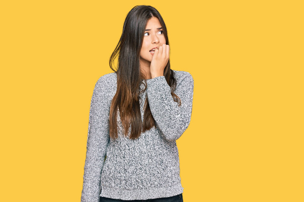Νεαρή μελαχρινή γυναίκα φορώντας casual πουλόβερ χειμώνα αναζητούν τόνισε και νευρικό με τα χέρια στο στόμα δαγκώνει τα νύχια. πρόβλημα άγχους.  - Φωτογραφία, εικόνα