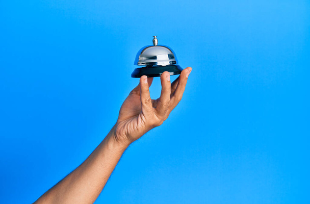 Young hispanic hand holding alarm bell over isolated blue background. - Foto, Imagen