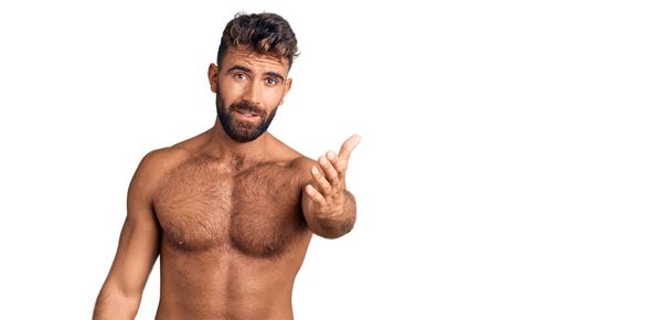 Jonge Spaanse man draagt zwemkleding zonder shirt lachend vriendelijk aanbieden van handdruk als groet en gastvrij. succesvol zakendoen.  - Foto, afbeelding