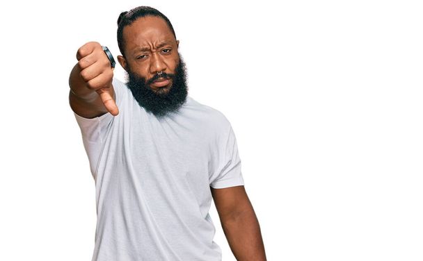 Young african american man wearing casual white tshirt looking unhappy and angry showing rejection and negative with thumbs down gesture. bad expression.  - Photo, Image