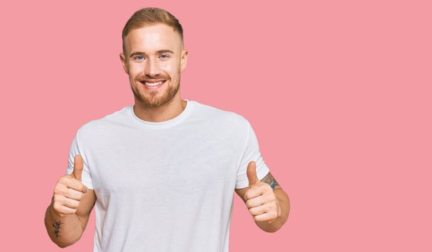 Young irish man wearing casual clothes success sign doing positive gesture with hand, thumbs up smiling and happy. cheerful expression and winner gesture.  - Фото, изображение