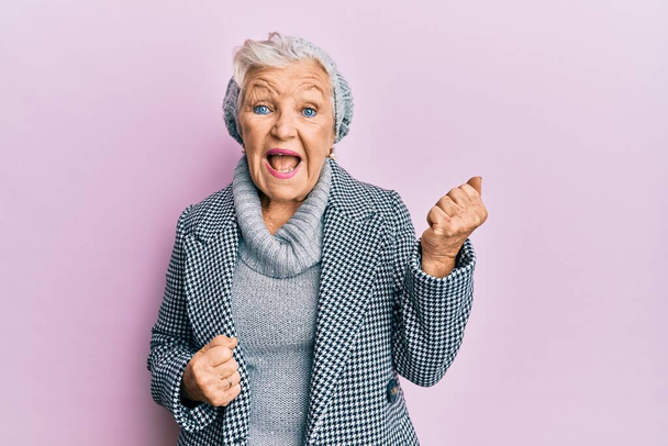 Senior harmaa tukka nainen yllään villa talvi villapaita juhlii yllättynyt ja hämmästynyt menestystä kädet ylhäällä ja silmät kiinni  - Valokuva, kuva