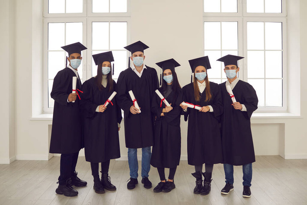 Portrét úspěšných studentů s diplomy v rukou a s lékařskými maskami na tvářích. - Fotografie, Obrázek