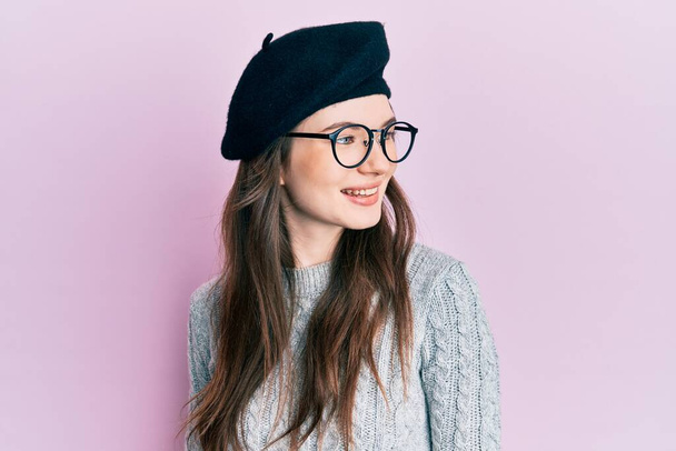 Młody piękny biały dziewczyna noszenie francuski wygląd z beret patrząc na bok, relaks profil pozować z naturalną twarz i pewny uśmiech.  - Zdjęcie, obraz