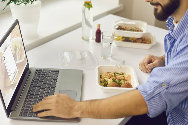 Mies ilmoittautuu elintarvikkeiden toimitus verkkosivuilla kannettavan tietokoneen kun lounas tauko toimistossa - Valokuva, kuva