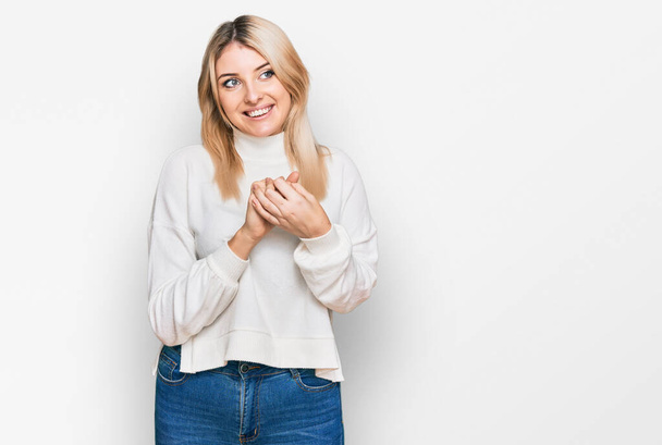 Молода біла жінка в повсякденному зимовому светрі сміється нервово і схвильована руками на підборідді дивиться в бік
  - Фото, зображення