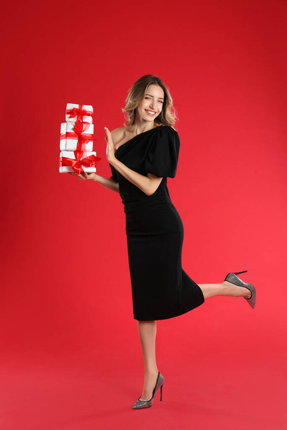 Beautiful young woman with Christmas presents on red background - Photo, image