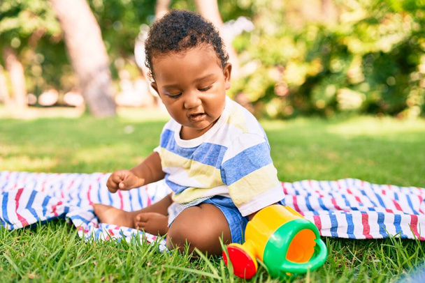 Adorable african american chubby toddler playing with toy sitting on the grass at the park. - Foto, Imagem