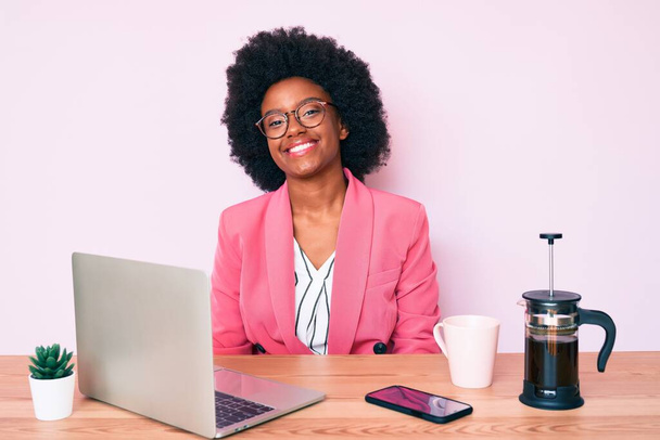 Mujer afroamericana joven que trabaja en el escritorio usando computadora portátil con una sonrisa feliz y fresca en la cara. persona afortunada.  - Foto, Imagen