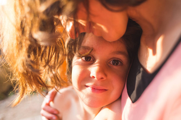 Portrait of a child hugging a mother, a boy spends time with mom, a woman gently hugs her son. Cute boy looks at his beloved mother. Sunset light passing through the hair. - Photo, image