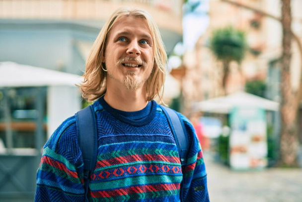 młody skandynawski student człowiek uśmiechnięty szczęśliwy stojąc w mieście. - Zdjęcie, obraz